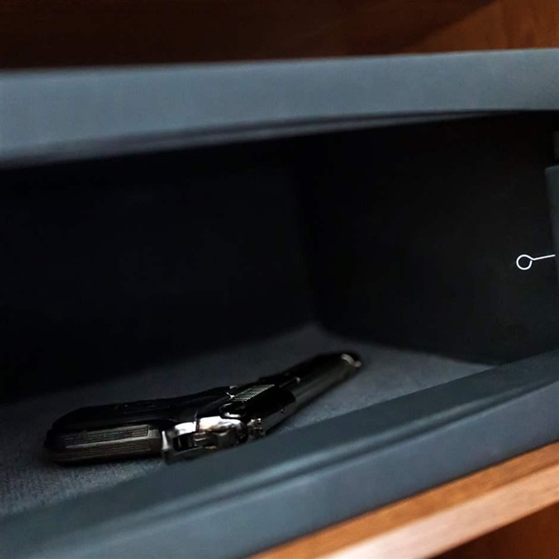  A handgun lies inside an open metal safe on a wooden shelf.