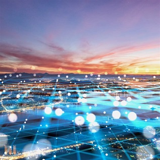 Cityscape verlaid with a bluish translucent network of grid lines and dots. In the distance, shadowed mountains rise beneath a colorful sunset sky.