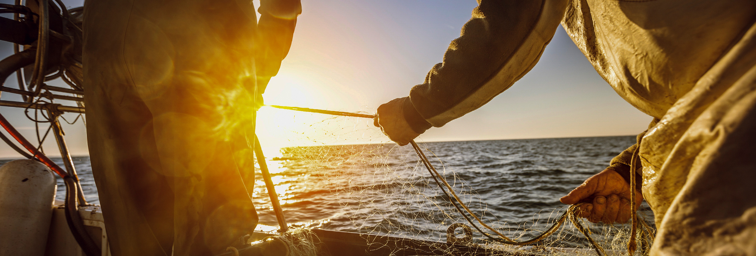 fisherman tying nets on board a boat with sun in background