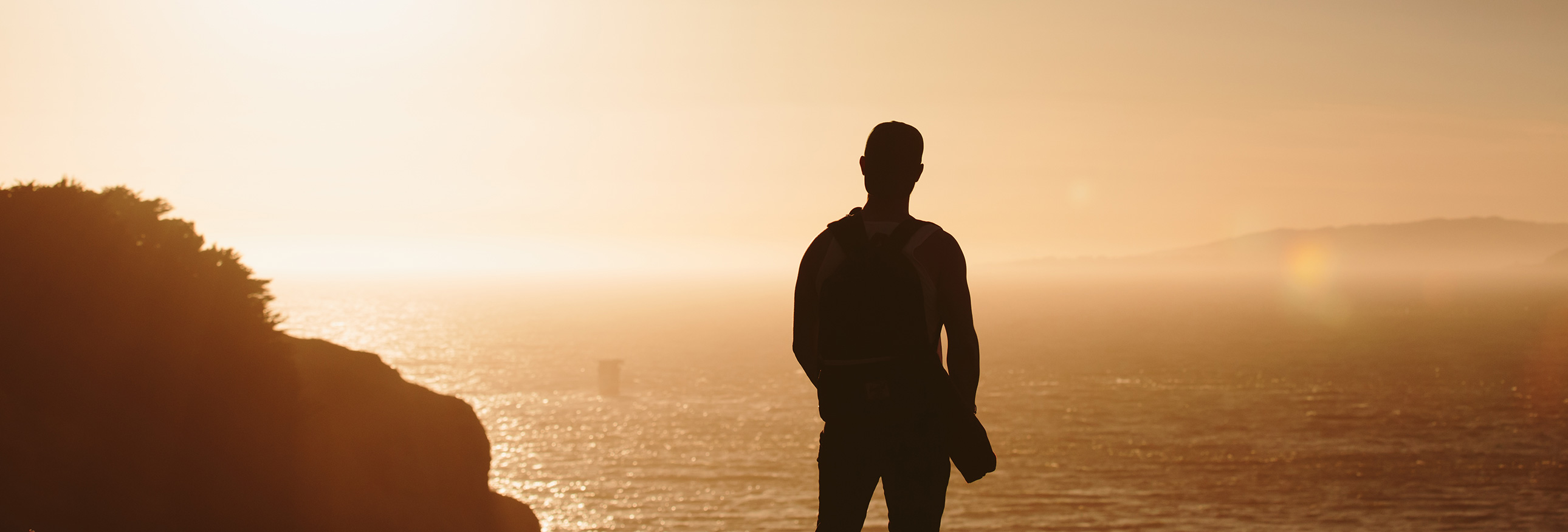 silhouette of a man overlooking water at sunset