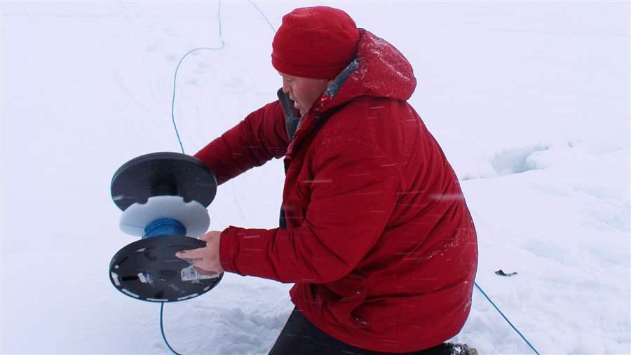 Alex Ootoowak unwinds more than 150 metres of rope before deploying the first hydrophone through the ice in Milne Inlet.
