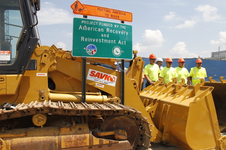Constructions equipment with wokers and a sign for the American Recovery and Reinvestment Act