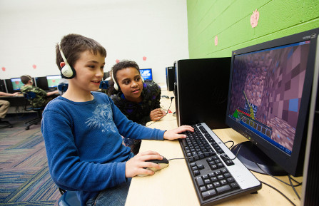 young boy and girl with headphones sit in front of computer