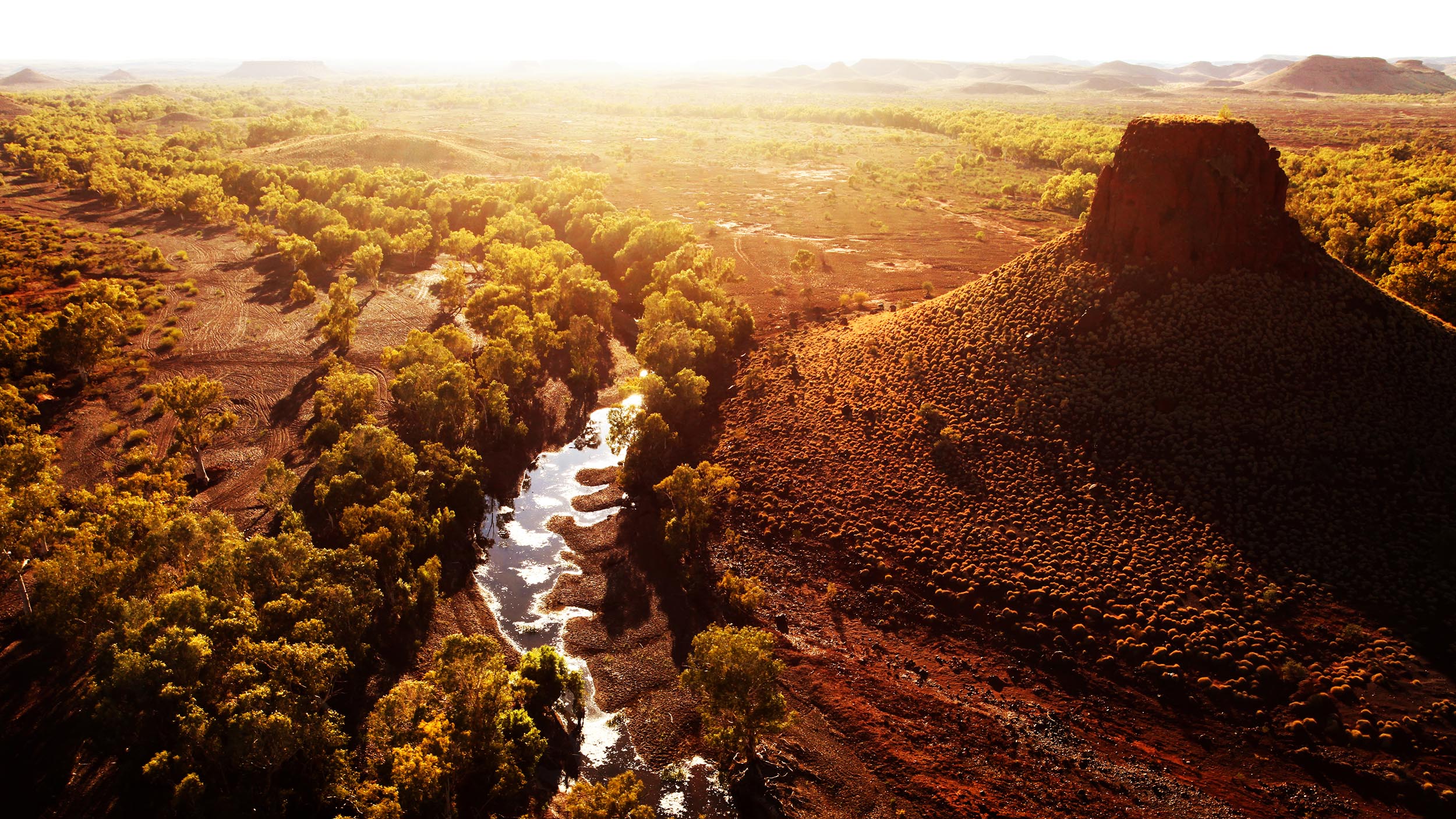 The sun sets behind Pannawonica Hill and the Robe River in Western Australia’s Pilbara region. Across much of the Outback, watercourses such as this ephemeral river, which is reduced to a series of permanent pools during the dry season, serve as important refugia for native animals and harbour distinctly different plant and animal communities.