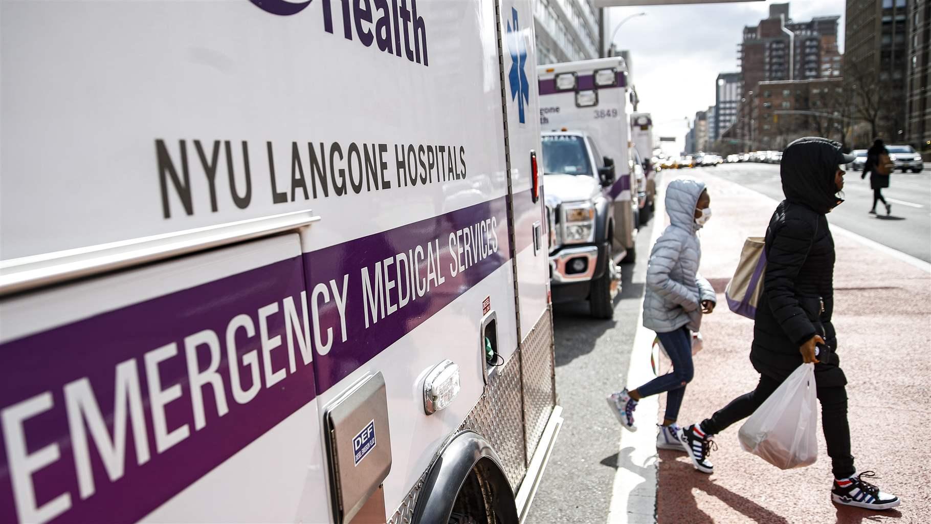 mask walks past a line of ambulances outside the NYU Langone Hospital Emerg...