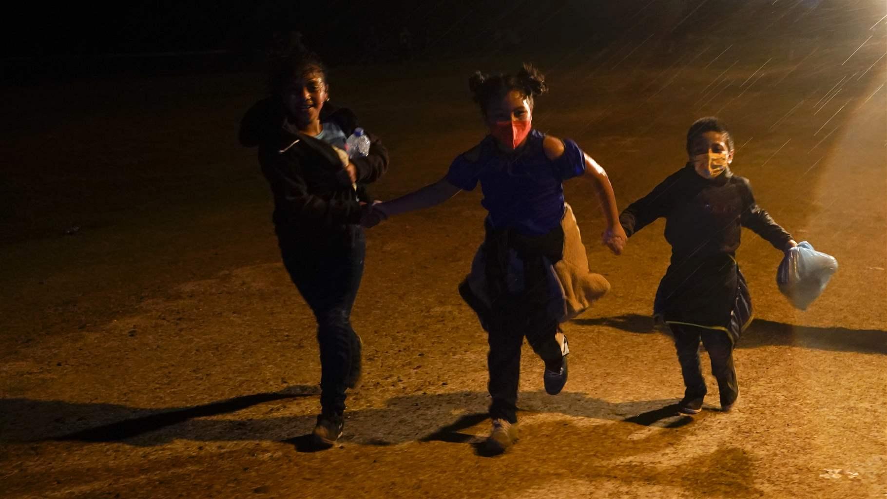 APTOPIX IMMIGRATION BORDER CROSSINGS Three young migrants hold hands as they run in the rain at an intake area after turning themselves in upon crossing the U.S.-Mexico border Tuesday, May 11, 2021, in Roma, Texas.