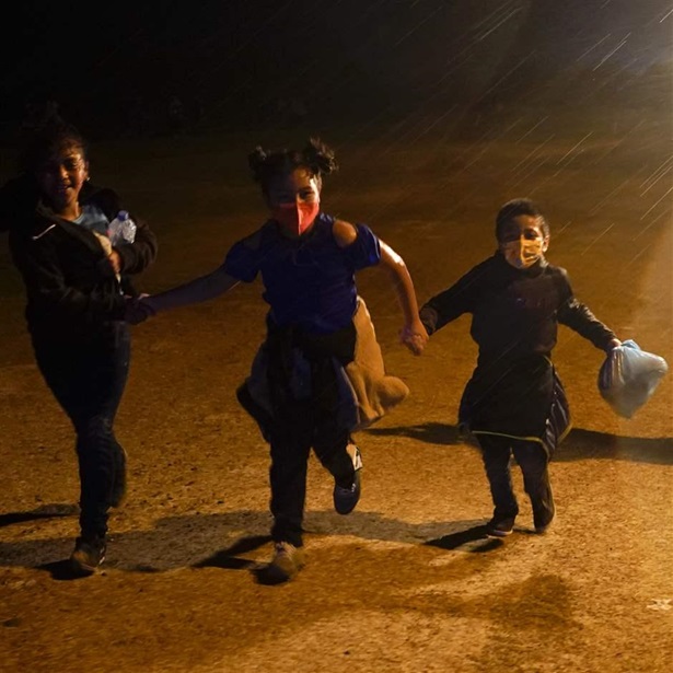 Three young migrants hold hands as they run in the rain at an intake area after turning themselves in upon crossing the U.S.-Mexico border Tuesday, May 11, 2021, in Roma, Texas.