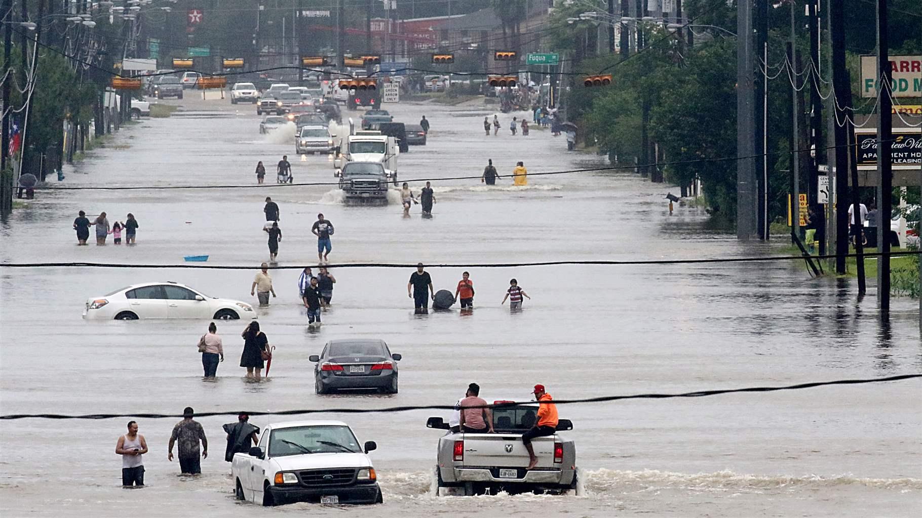 People walk through the flooded waters of Telephone Rd. in Houston on August 27, 2017 as the US fourth city city battles with tropical storm Harvey and resulting floods. 