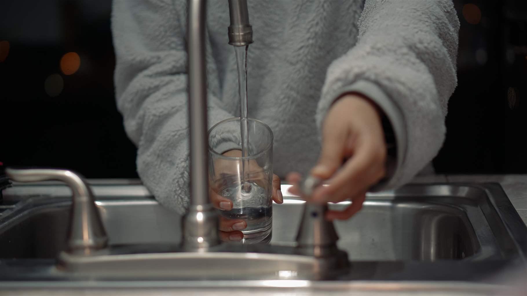person filling up water glass in sink