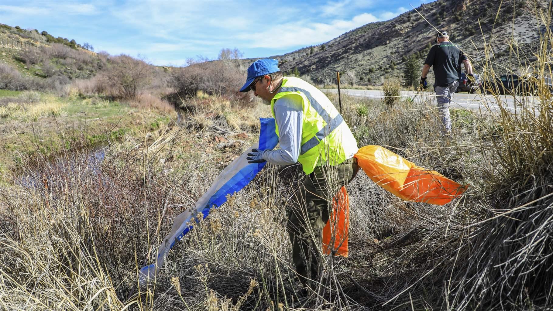 John Packer, owner of Fly Fishing Outfitters, grabs a plastic bag during the annual highway cleanup Saturday, May 1, 2021 near Wolcott, Colo. Packer said every year they play a game to find the most common beer bottle or can.