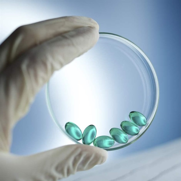 A gloved hand holding a petri dish with green prescription pills