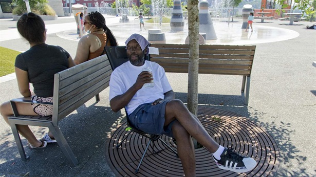 Melvin O'Brien waits in the shade in Yesler Terrace Park while his children play in the spray park during a heat wave hitting the Pacific Northwest, Sunday, June 27, 2021, in Seattle.