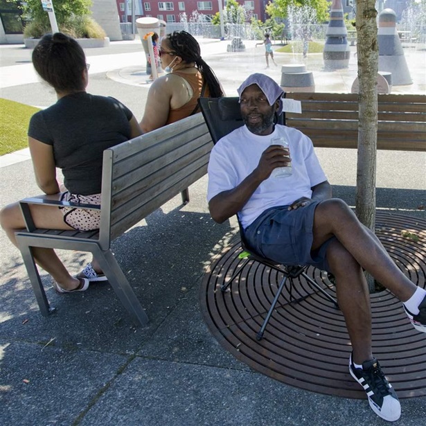 Melvin O'Brien waits in the shade in Yesler Terrace Park while his children play in the spray park during a heat wave hitting the Pacific Northwest, Sunday, June 27, 2021, in Seattle.