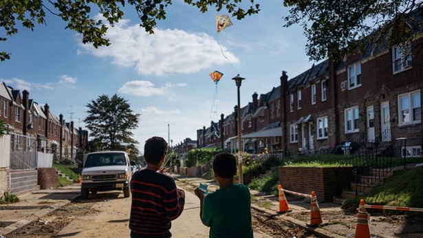 Two young boys facing back fly kites in a eroded neighborhood with construction signs, a truck, and unfinished roads