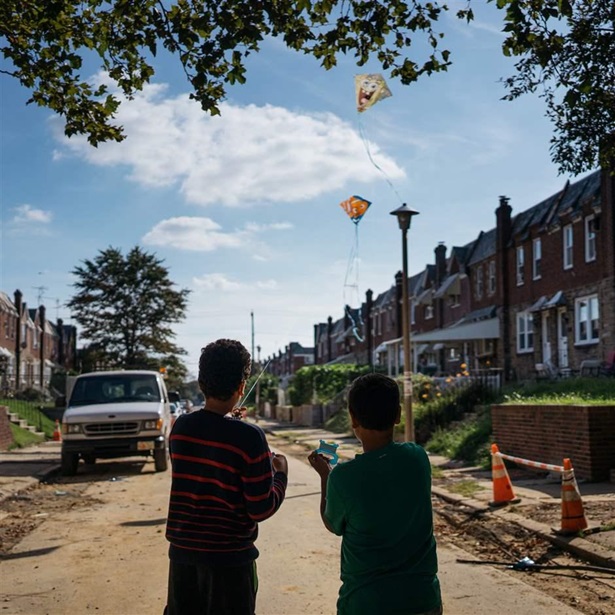 Two young boys facing back fly kites in a eroded neighborhood with construction signs, a truck, and unfinished roads