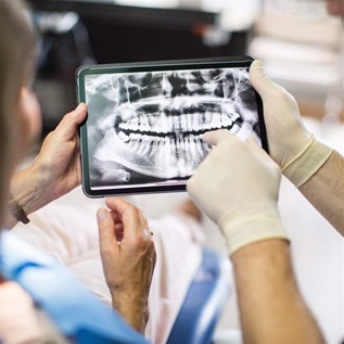 Cropped shot of dentist showing teeth x-ray image on digital tablet screen to female patient at dental clinic. Dentist and patient looking at teeth x-ray on a digital tablet.