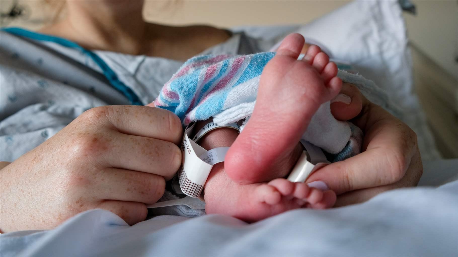 Newborn Infant Baby Boy Feet Wrapped In Blanketwith Partial Shot Of Mother And Her Hands