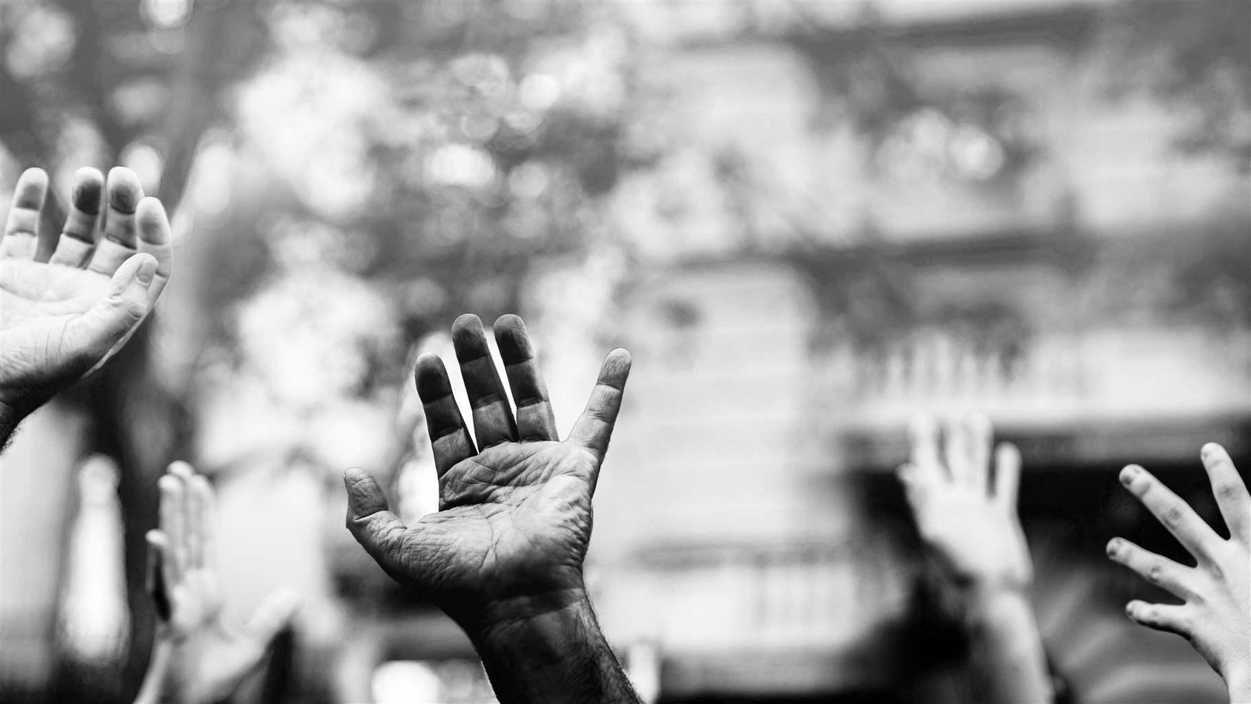 Black and white photo of hands of diverse skin colors raised in the air.