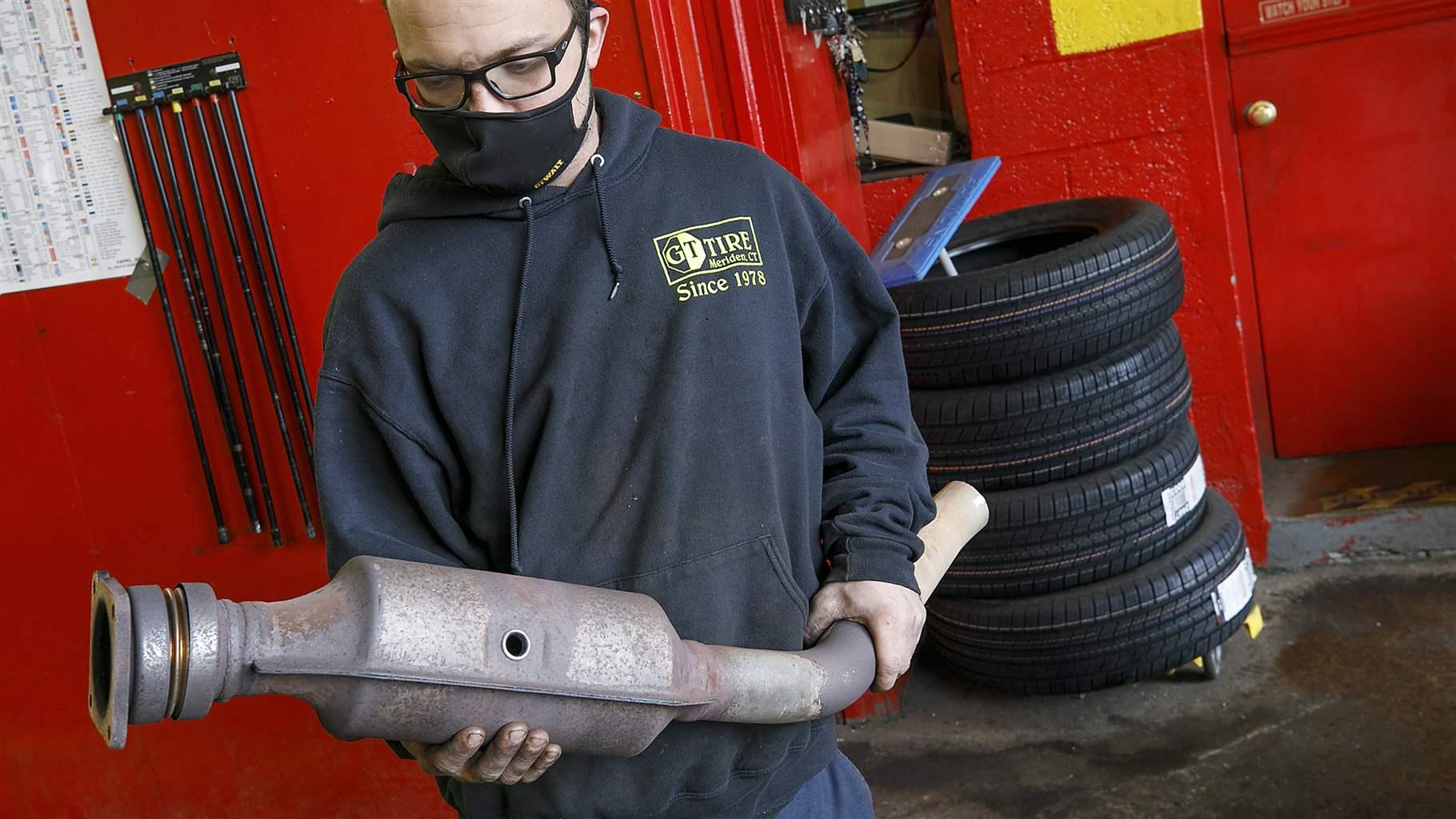 Ari Thielman, manager at GT Tire & Service Center in Meridien, Conn., holds a catalytic converter from a Ford F-150 that the business replaced for a customer. Catalytic converter theft has skyrocketed in the past few years, and legislatures are trying to address the problem