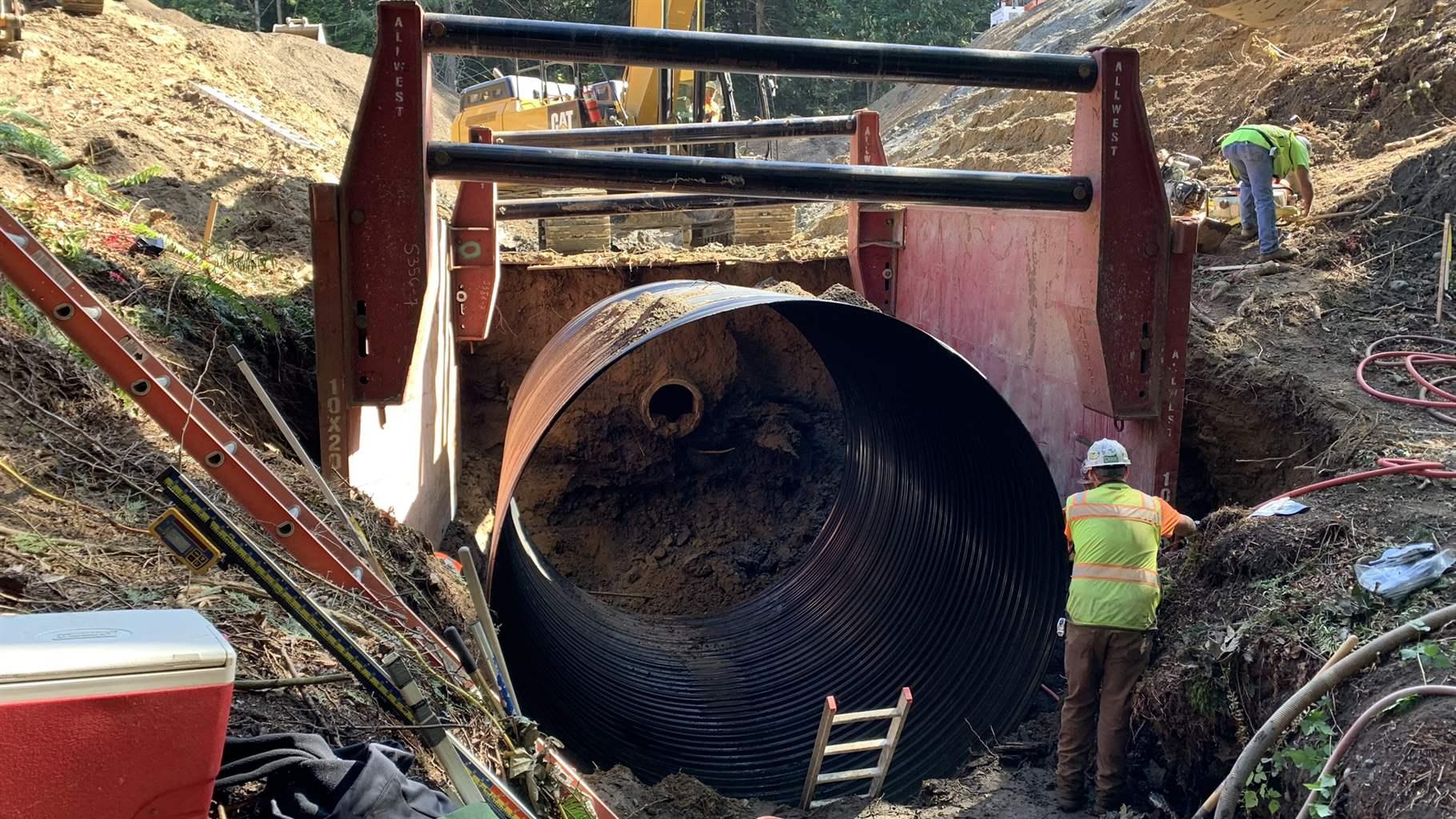 A construction crew in a large ditch replaces an old culvert. 