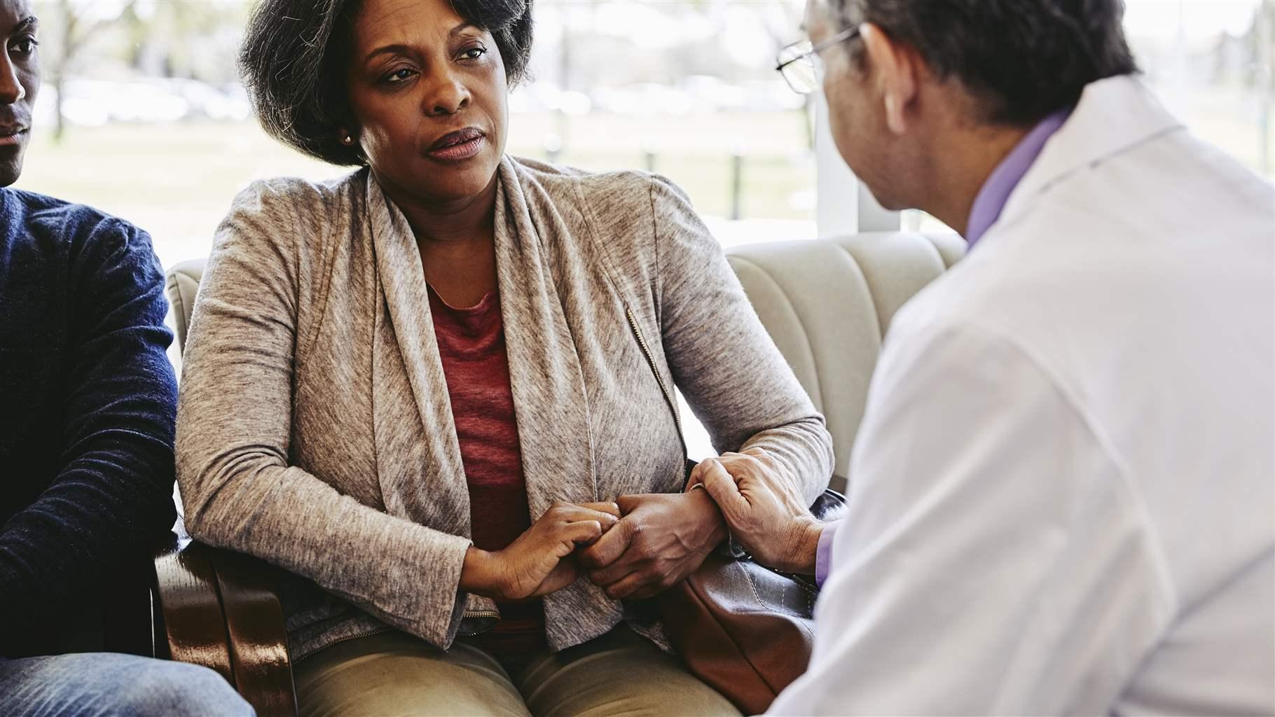 Male doctor consoling mature woman sitting with son in hospital lobby