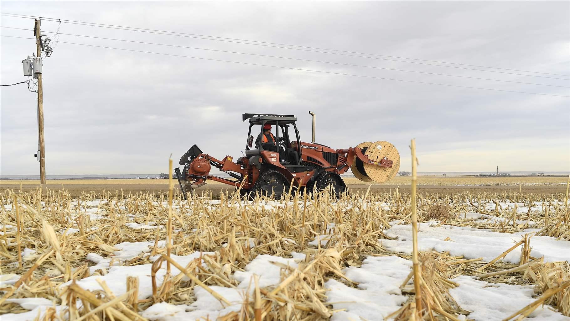 A tractor is digging a trench in a lightly snow covered field. 