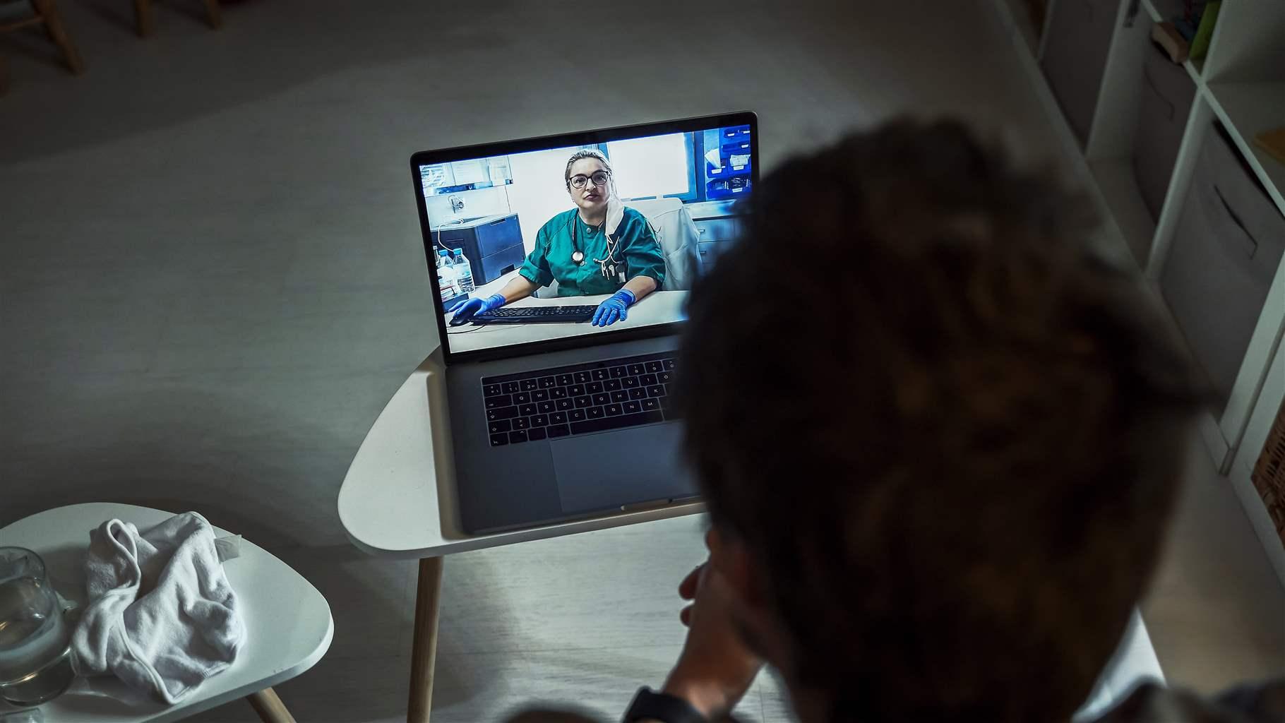 Rear view of man consulting doctor over laptop in living room at home