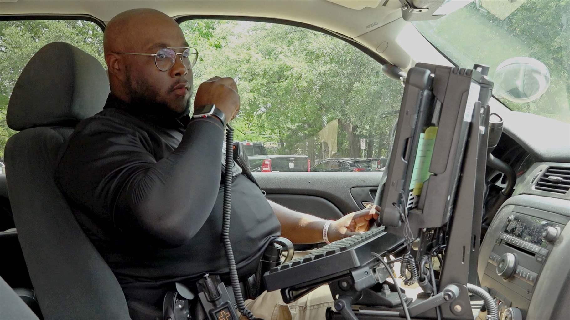 Dallas Police Officer Kelsey Banks holding a walkie talkie on his left while in a police car