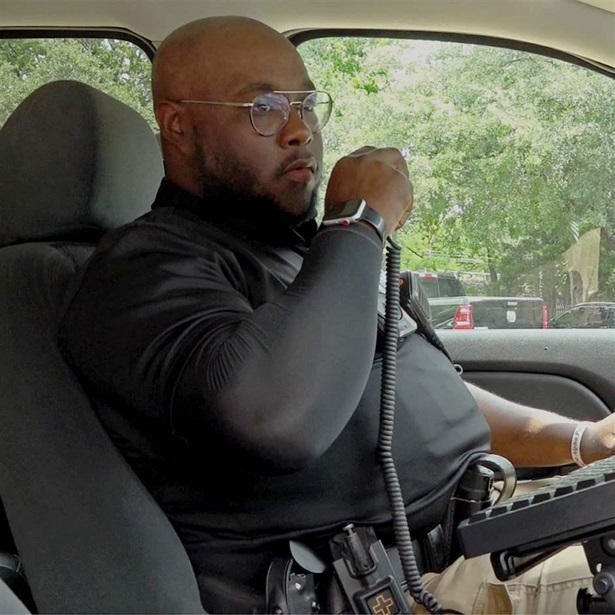 Dallas Police Officer Kelsey Banks holding a walkie talkie on his left while in a police car