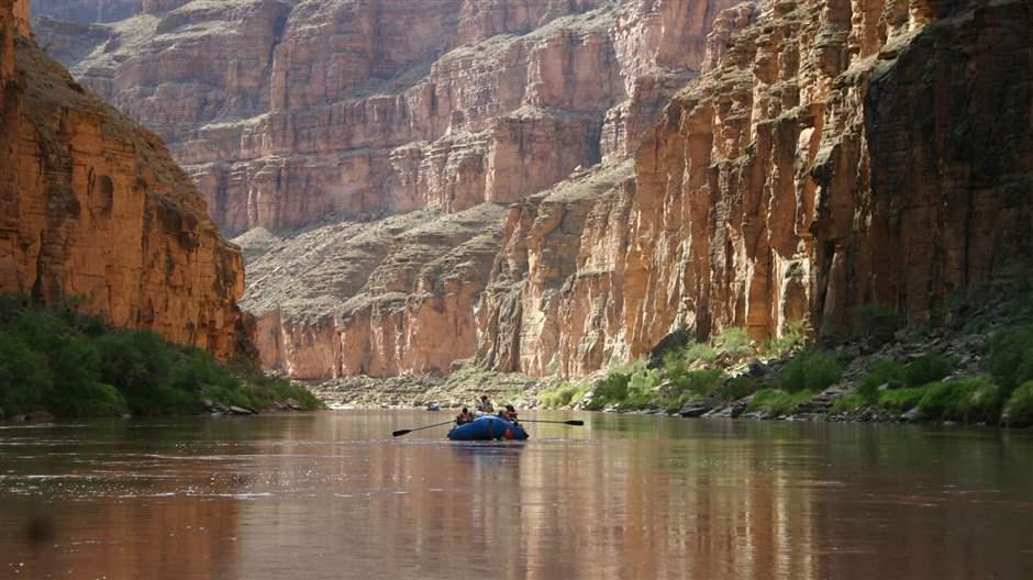 A raft floating down the middle of the Colorado River with cliff on either side. 