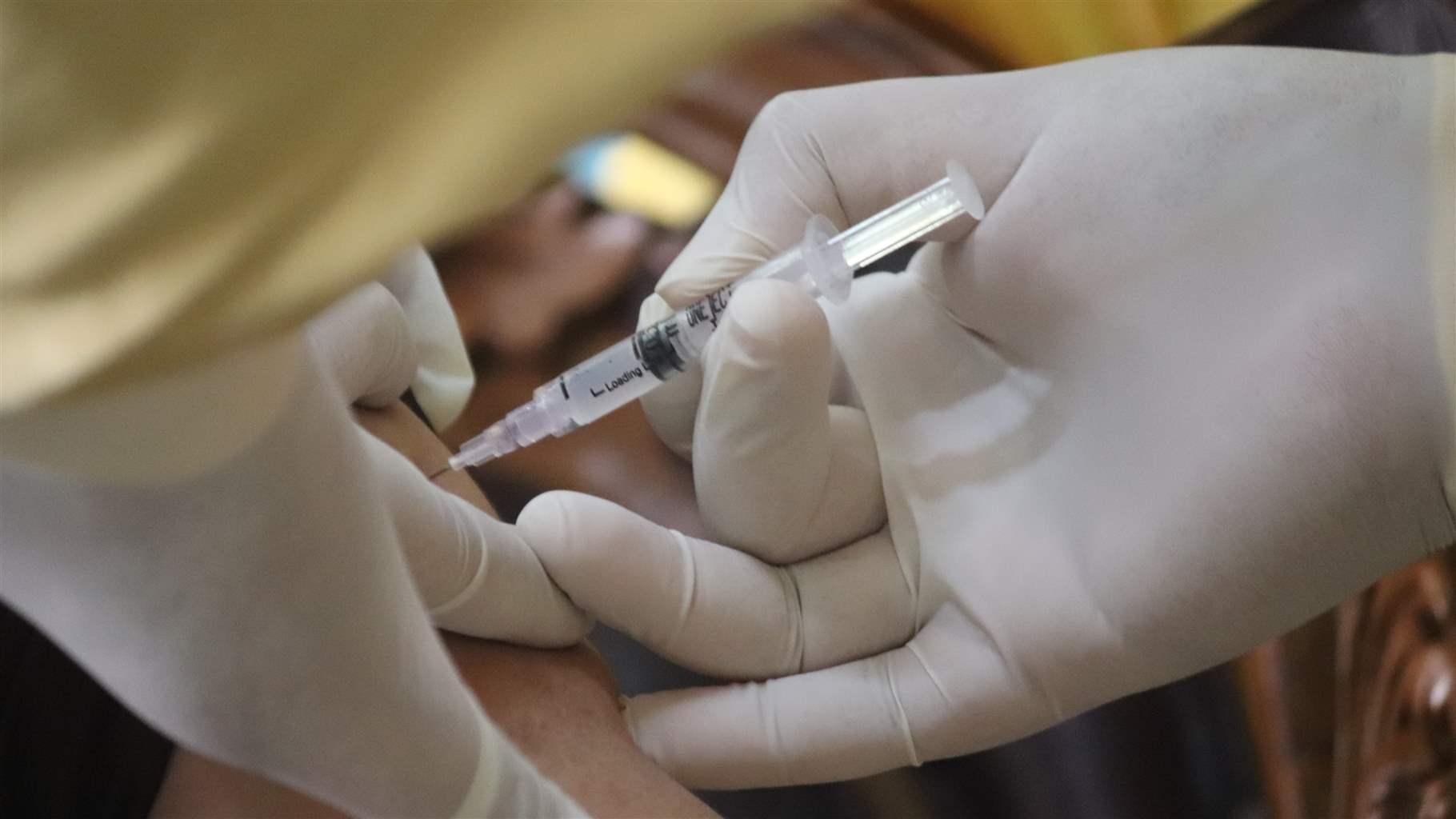 Closeup of two gloves hands inserting a syringe for injection into an arm
