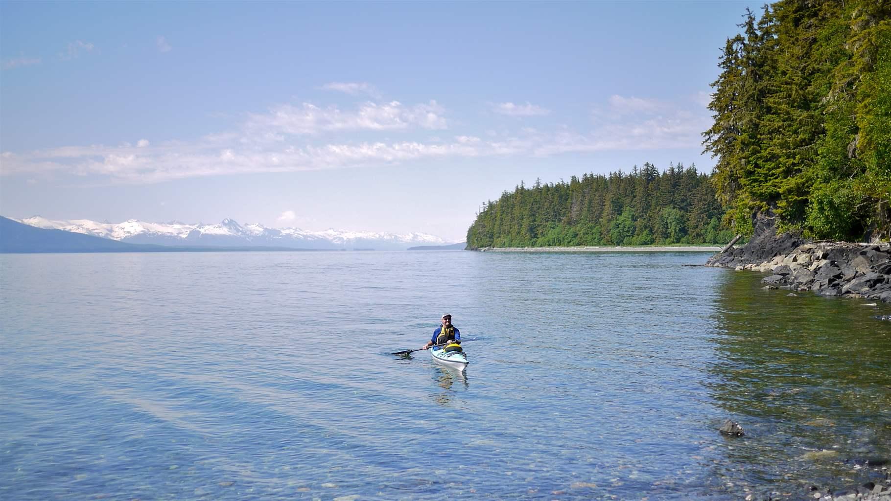A kayaker paddles toward Douglas Island with snowcapped mountains in the distance. 