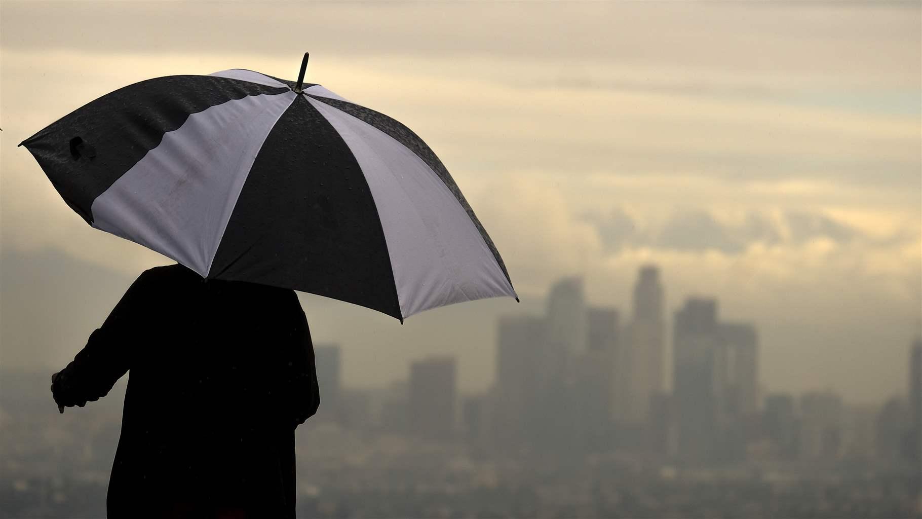 Clouds over LA A person with an umbrella looking over a cloud cover Los Angeles in the distance.
