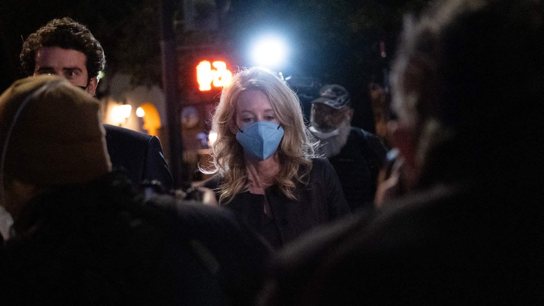 Elizabeth Holmes walking out of federal court at night with a mask and a crowd around her. 