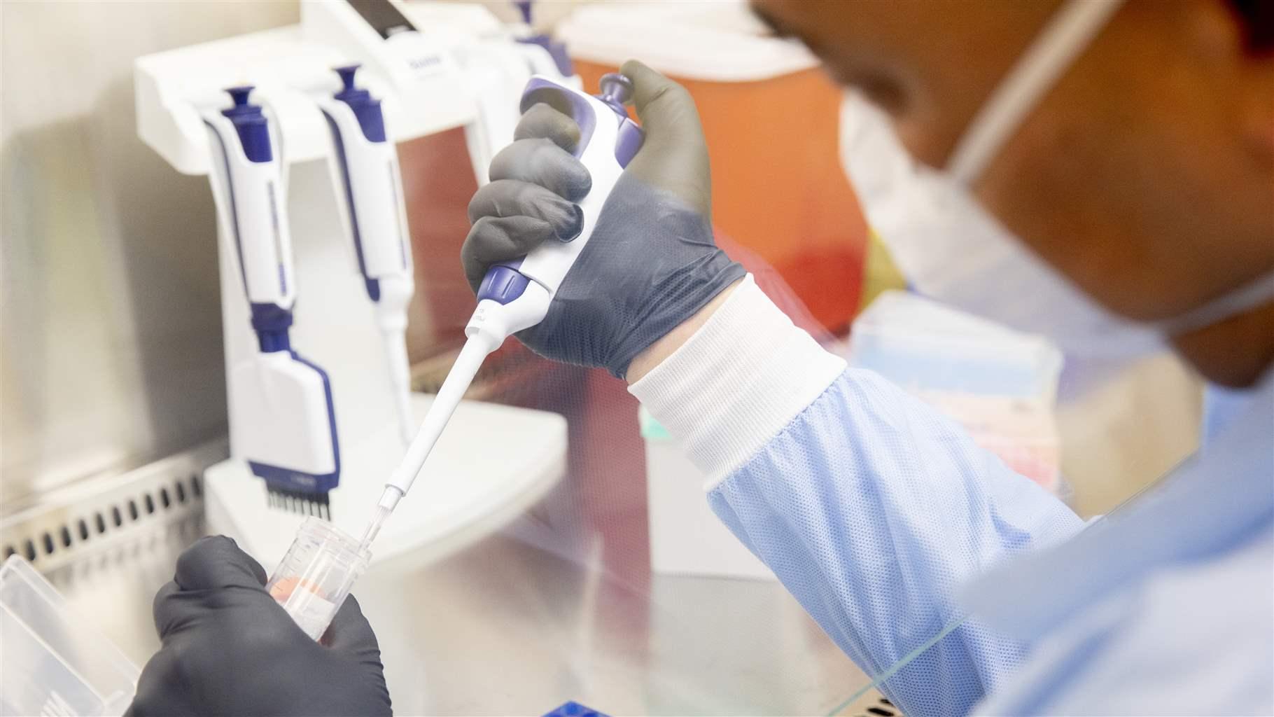 A person in medical scrubs and gloves is extracting samples from a tube with a syringe.