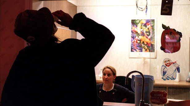 A patient in profile at a methadone clinic with a cup to their mouth in front of an office desk.