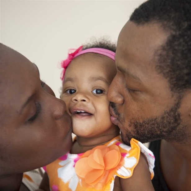 Side profiles of a mother and father kissing the cheeks a baby girl who is in the middle