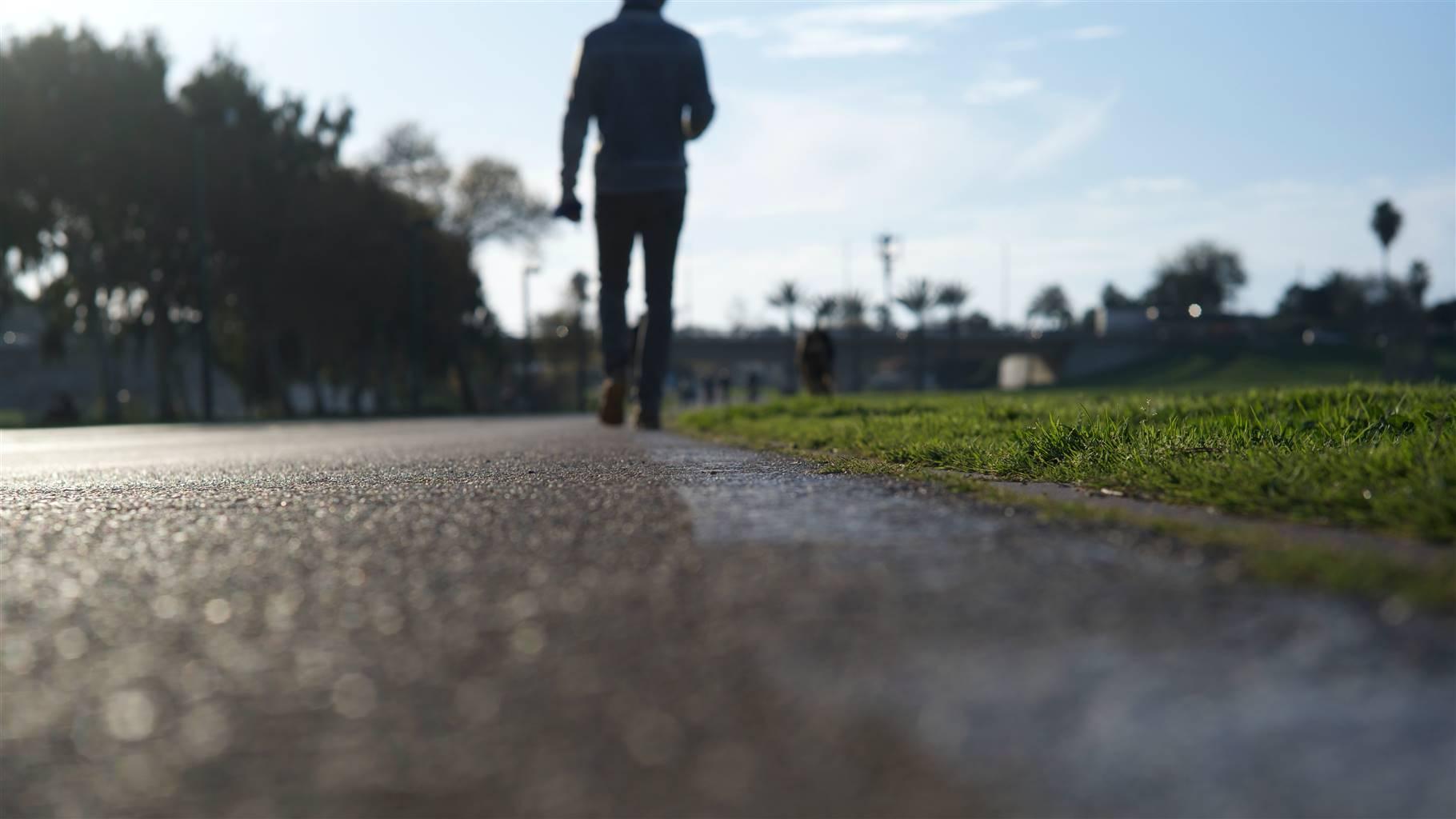 A landscape shot of a person&#39;s back walking on a pavement