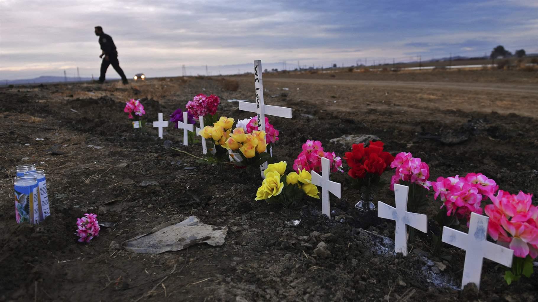 Seven small crosses and one large one create a memorial along Highway 33 as California Highway Patrol officers survey the scene a day after a fatal crash the night before, 13 miles south of Coalinga, Calif., Saturday, Jan. 2, 2021.