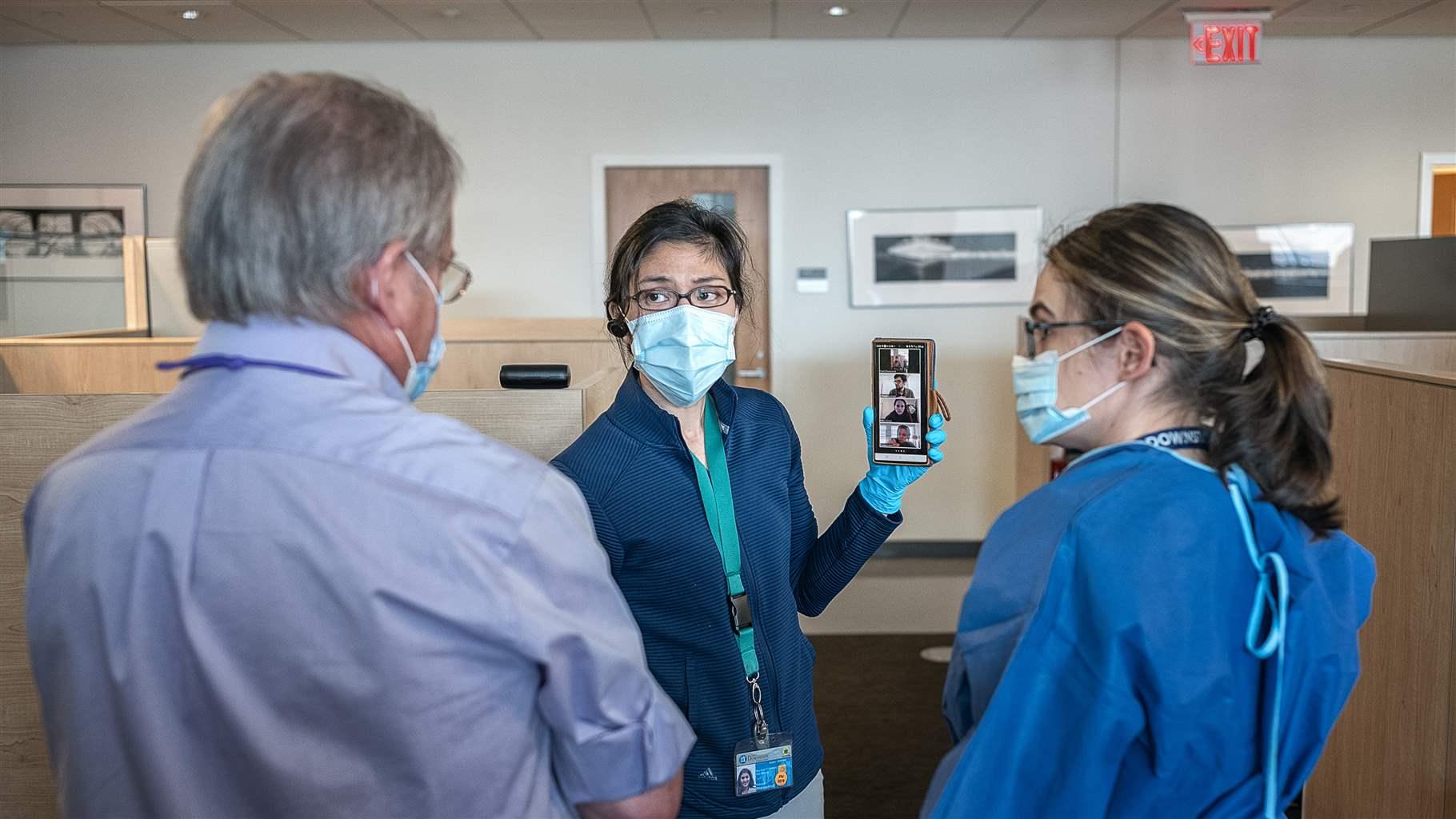 A Mirimus Lab executive and Downstate researchers have a Zoom meeting with AI/App developers on April 20, 2020 in New York City. A group of medical professionals gather around a handheld medical device.