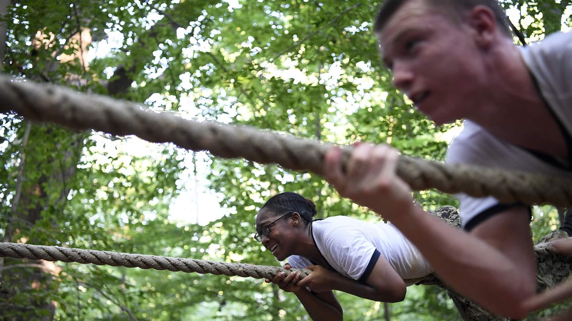 U.S. Naval Academy recruits climb along a rope on an obstacle course. 