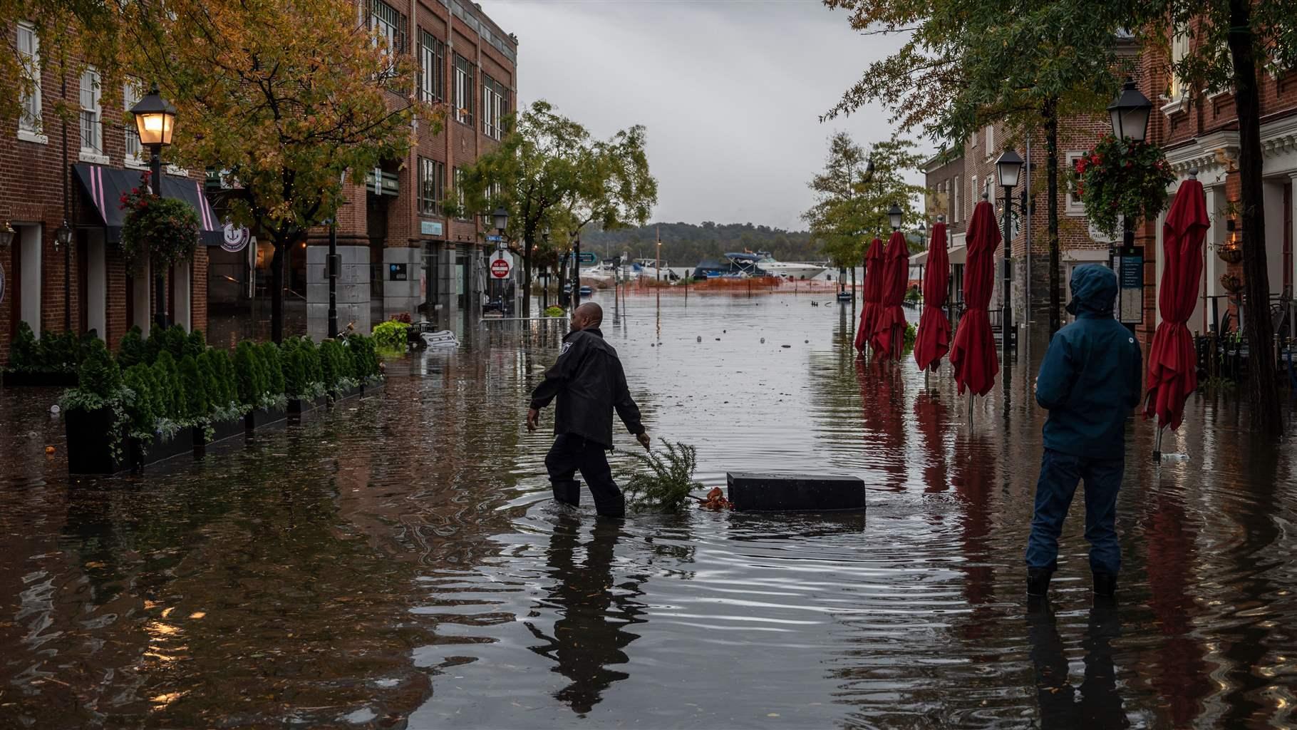 A police officer pulls a potted plant across a flooded street near a bar in Old Town Alexandria, Virginia, on October 29, 2021.