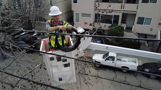 Sonic technician Tom Sherrill works on securing the cable to the utility wires through branches as he installs fiber optic cable to a home in Berkeley, Calif., on Monday, March 4, 2019.