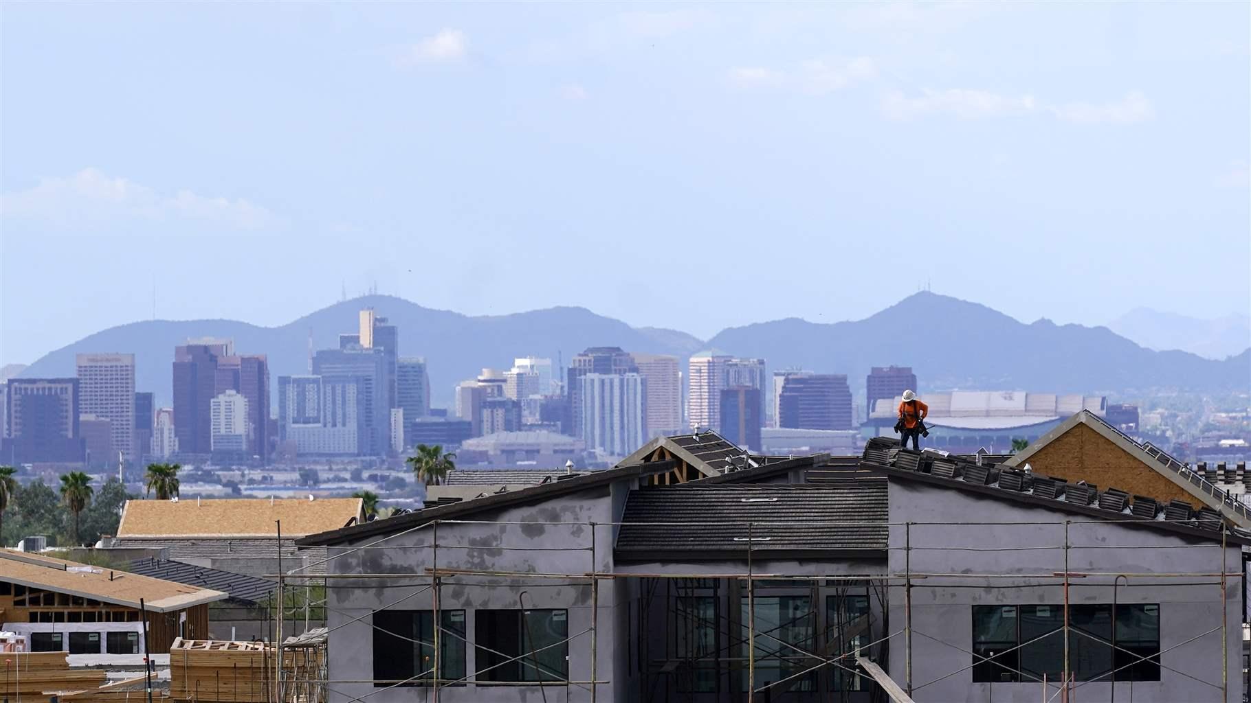 A construction worker on a roof with a city and mountain skyline in the distance. 
