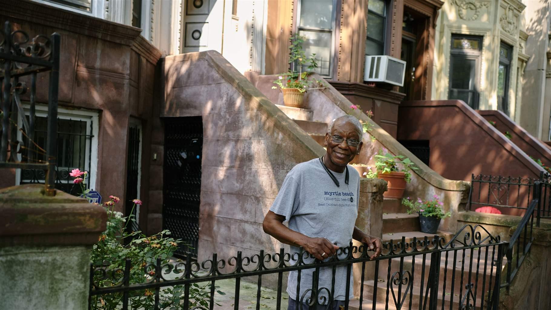 A homeowner standing at the iron fence in front of his row house.