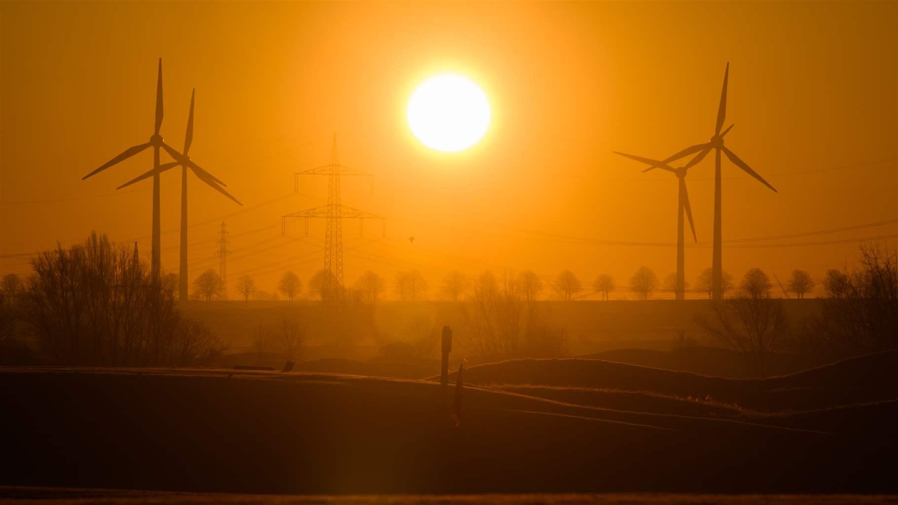 The sun rises between wind turbines and a high-voltage power line in the Hannover region. 
