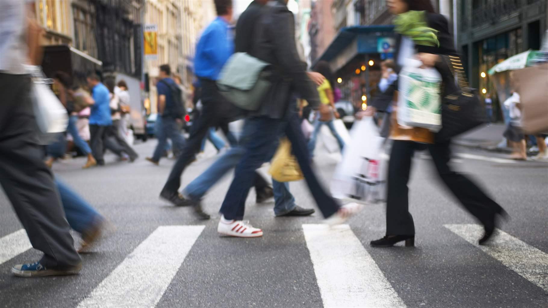 Pedestrians walking across a crosswalk on a busy New York City street.
