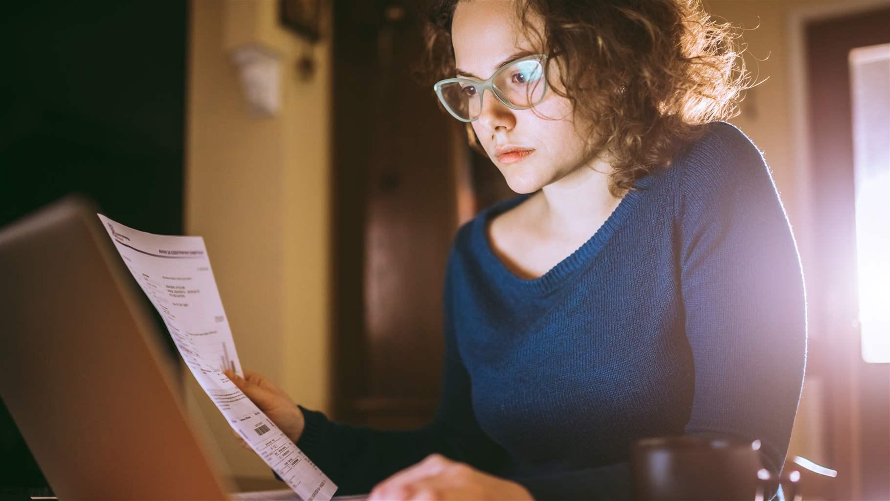 Young brunette curly female reading her bill papers, looking stressed