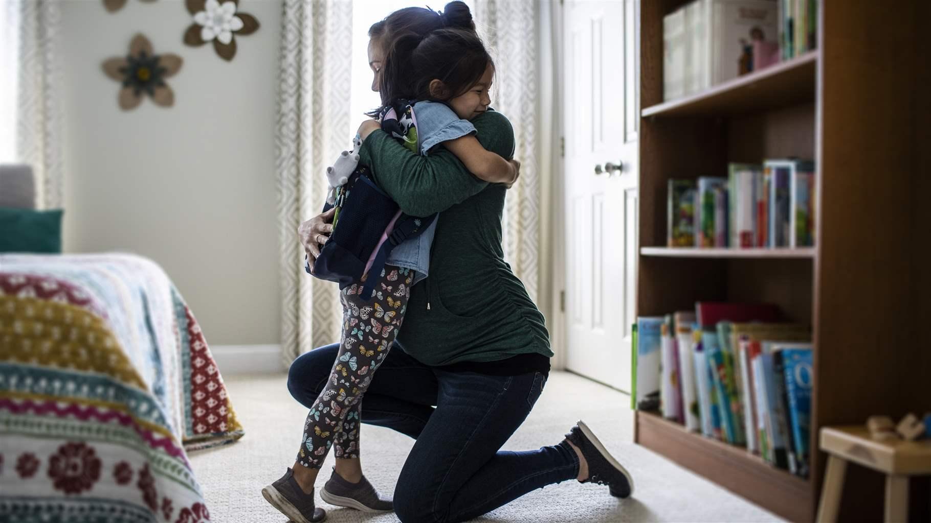 Mother embracing young daughter before school