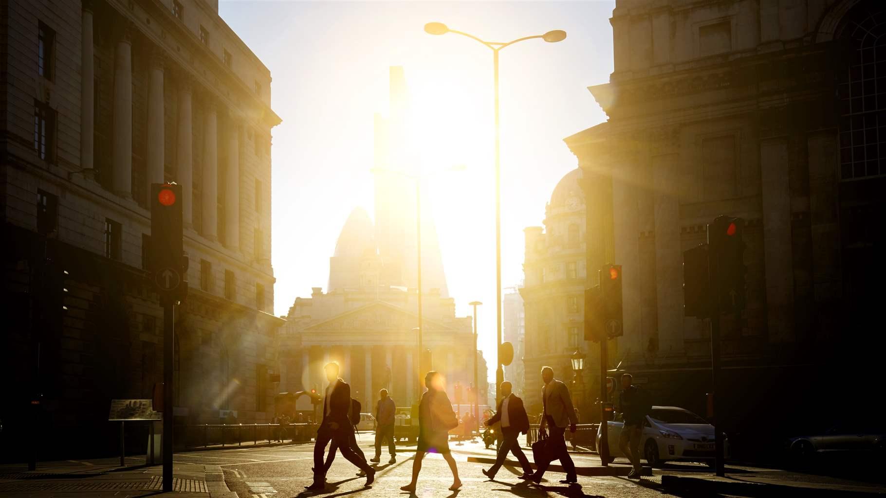 Pedestrians walking to work through the city at sunrise with rays of sun braking over the capitol building.